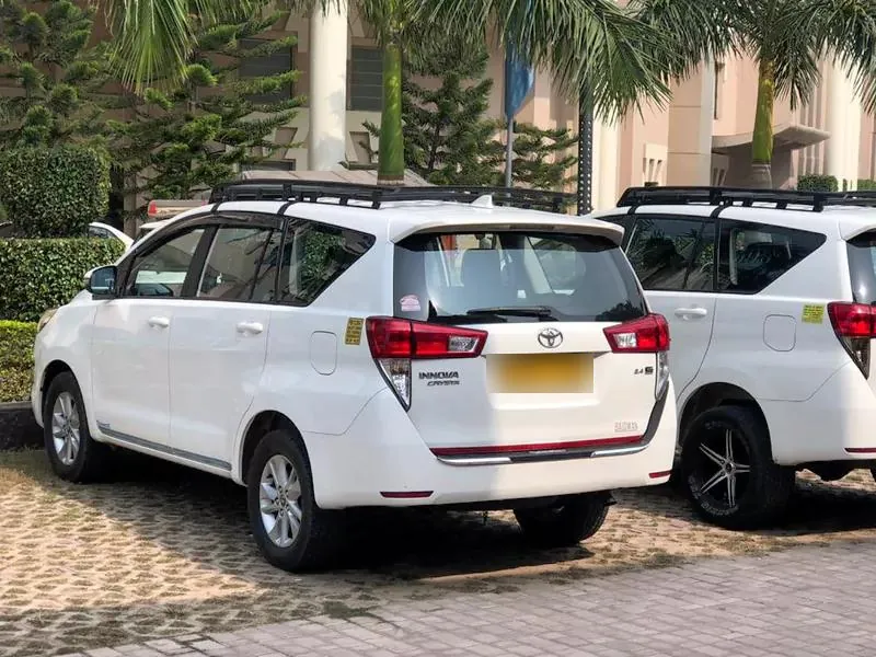 Two white Innova Crysta cars with roof carriers ready for an outstation family trip